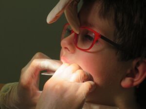 A kid at the dentist getting some work done under a light with a person adjusting his glasses